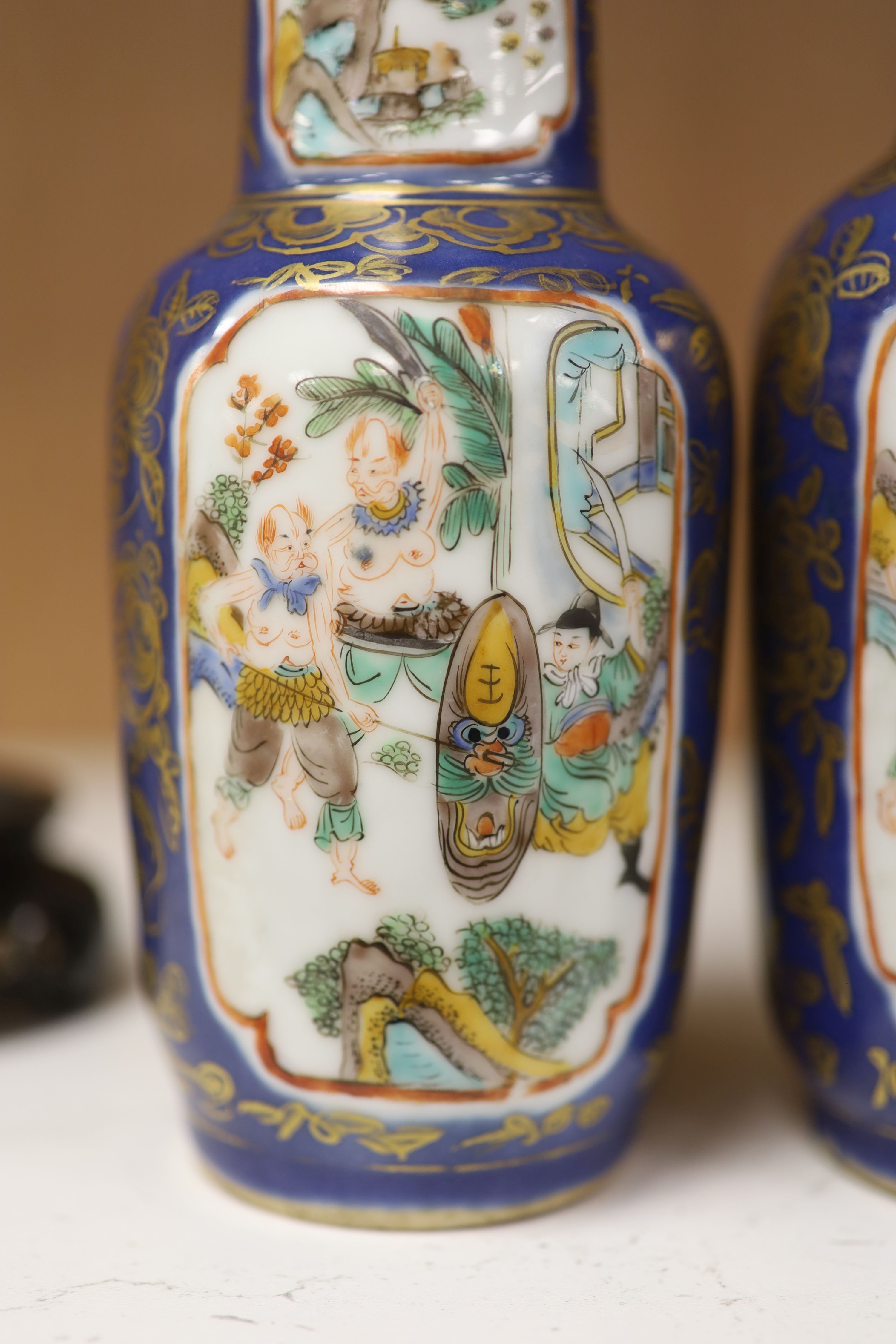 A pair of Chinese Kangxi style blue-ground vases, late 19th century decorated with panels of warriors and heightened in gilt, on carved hardwood stands, height 18cm excluding stand